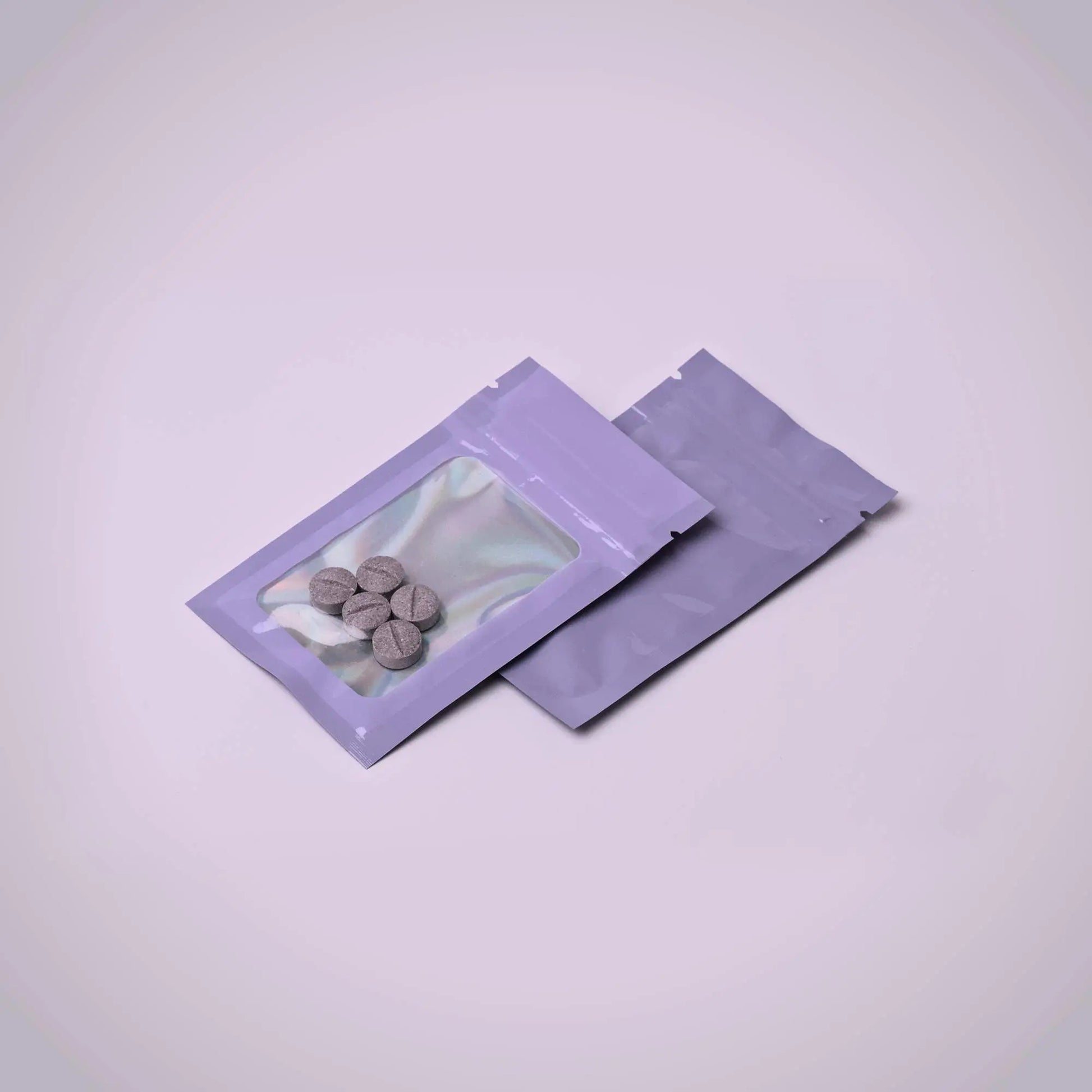 Two purple transparent packaging pouches with small 7ohBLACK 7-oh items inside on a light purple background